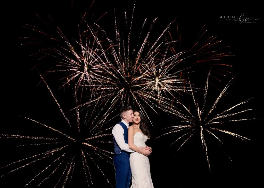 Bride and groom posing underneath firework display